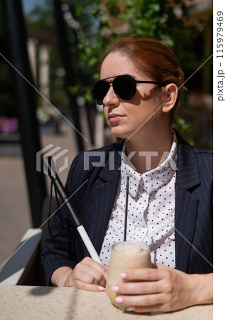 Blind woman in business suit drinking ice coffee in outdoor cafe. Blind woman in business suit drinking ice coffee in outdoor cafe. 115979469