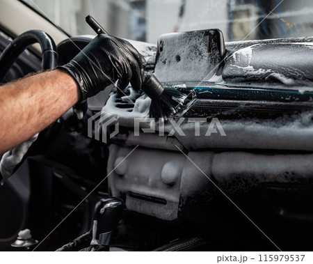 A mechanic cleans the interior of a car with a brush and foam. A mechanic cleans the interior of a car with a brush and foam. 115979537