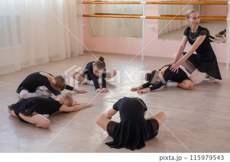 Caucasian woman and five little girls sit in a circle and do stretching at a ballet school. Caucasian woman and five little girls sit in a circle and do stretching at a ballet school. 115979543