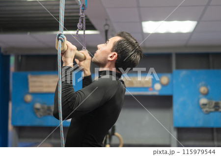 Caucasian man doing pull-ups on trapeze. Warm-up before the climbing wall.  115979544