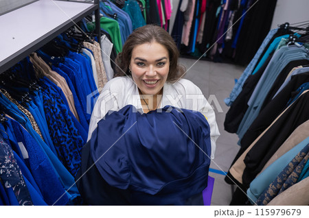 Top view of a chubby-cheeked woman holding an armful of clothes in a plus size store. Top view of a chubby-cheeked woman holding an armful of clothes in a plus size store. 115979679