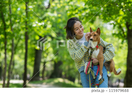 A young beautiful woman holds a dog in her arms for a walk. non-barking african basenji dog. A young beautiful woman holds a dog in her arms for a walk. non-barking african basenji dog. 115979688