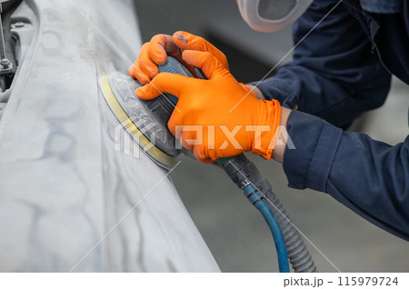 A mechanic sands the putty on a car body with a machine. Repair after an accident.  115979724