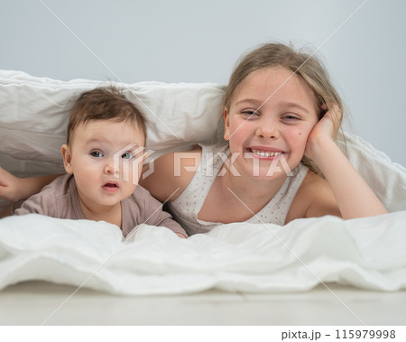 Little girl and her newborn brother hiding under the blanket.  115979998