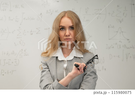 A Caucasian woman stands at a blackboard with written formulas. 115980075
