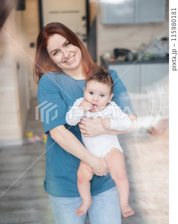 View through the window of a red-haired Caucasian woman holding her little son. Vertical photo. View through the window of a red-haired Caucasian woman holding her little son. Vertical photo. 115980181