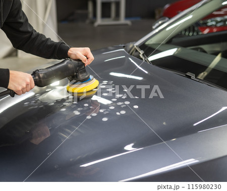A mechanic polishes the surface of the hood of a gray car.  115980230