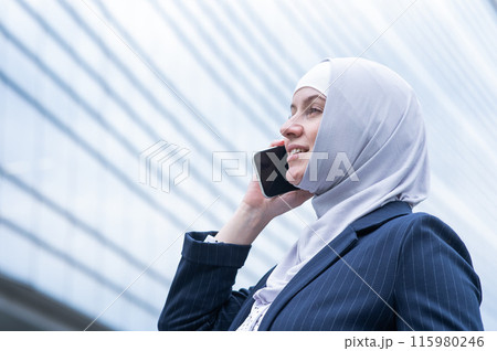 Business woman in hijab and suit talking on smartphone. Business woman in hijab and suit talking on smartphone. 115980246