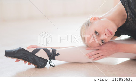 A young woman lies bent over on her feet in a ballet class. Ballerina stretches on the floor. A young woman lies bent over on her feet in a ballet class. Ballerina stretches on the floor. 115980636