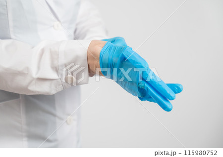 The doctor puts on latex gloves on a white background.  115980752