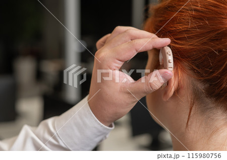Man putting hearing aid on Caucasian red-haired woman. Man putting hearing aid on Caucasian red-haired woman. 115980756