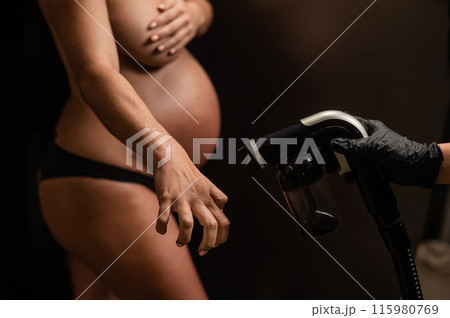 The master applies bronzer with a spray on the hands of a pregnant woman. Instant tan. The master applies bronzer with a spray on the hands of a pregnant woman. Instant tan. 115980769