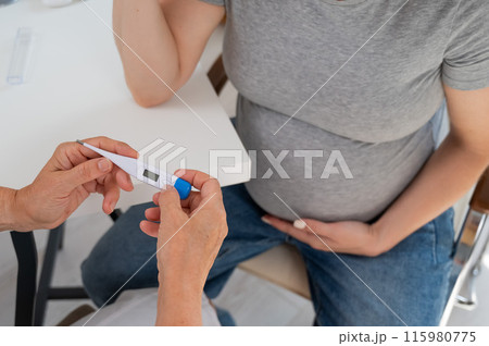 A pregnant woman visits a doctor. Therapist holding an electronic thermometer.  115980775