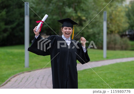 Caucasian woman in graduate gown dancing for joy outdoors. Caucasian woman in graduate gown dancing for joy outdoors. 115980776