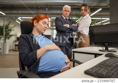 A pregnant woman sleeps at her workplace. Colleagues look disapprovingly.  115980787