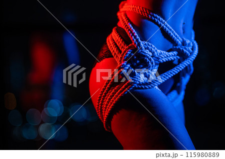 Close-up of a woman's belly in ropes tied using the Japanese shibari technique. Close-up of a woman's belly in ropes tied using the Japanese shibari technique. 115980889