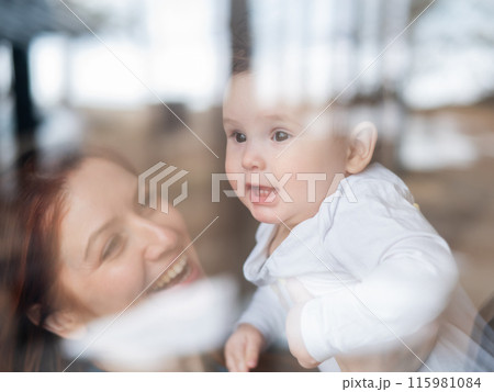 View through the window of a red-haired Caucasian woman holding her little son. View through the window of a red-haired Caucasian woman holding her little son. 115981084