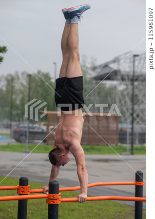 A young man doing a handstand on parallel bars outdoors. Workout. A young man doing a handstand on parallel bars outdoors. Workout. 115981097