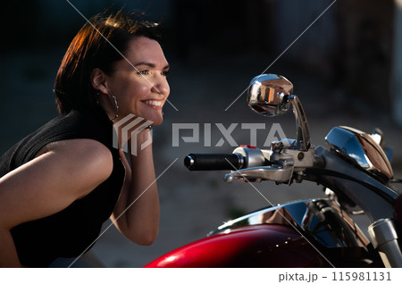 Brunette woman looks in the rearview mirror on a motorcycle. 115981131