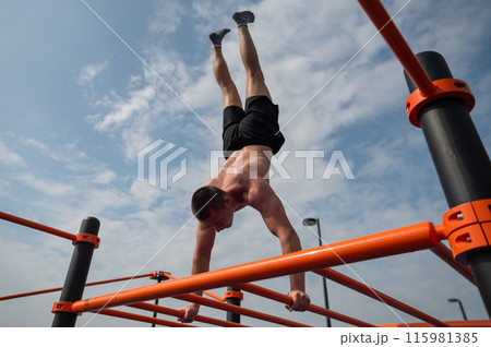 A young man doing a handstand on an outdoor sports field. Workout. A young man doing a handstand on an outdoor sports field. Workout. 115981385