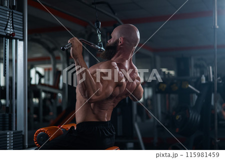 Caucasian man doing lat pull-downs on a machine. Caucasian man doing lat pull-downs on a machine. 115981459