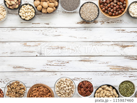Mixed assorted nuts and seeds in various bowls on white wooden table and space for text 115987460