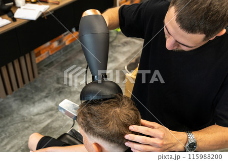 Barber drying his client's freshly treated hair with a blow dryer. Barber drying his client's freshly treated hair with a blow dryer. 115988200