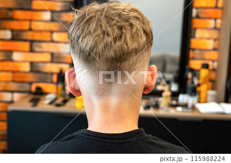 The picture of a small child in a barbershop studio, taken from behind and shows what a beautiful cut he has, the hair is blond. 115988224