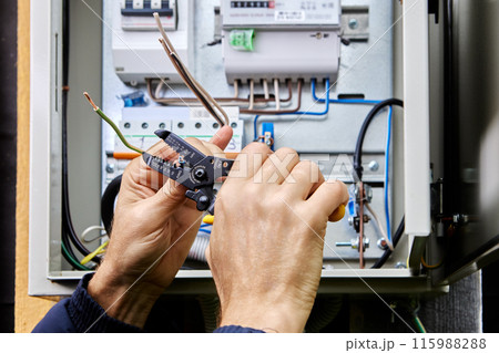Using stripping and wire cutting tool, an electrician connects three-phase power cable to an outdoor electrical cabinet. 115988288