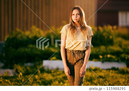 White woman in striped trousers against striped wall in garden at sunset. White woman in striped trousers against striped wall in garden at sunset. 115988291