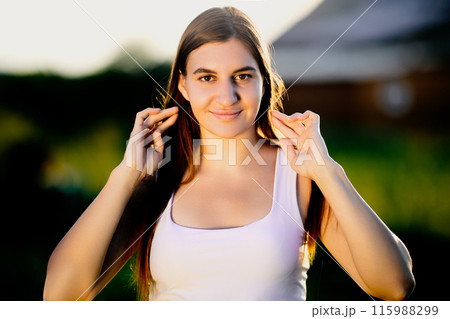 During golden hour, face of young Caucasian woman is illuminated by light of setting sun, outdoors portrait in countryside on summer evening. During golden hour, face of young Caucasian woman is illuminated by light of setting sun, outdoors portrait in countryside on summer evening. 115988299