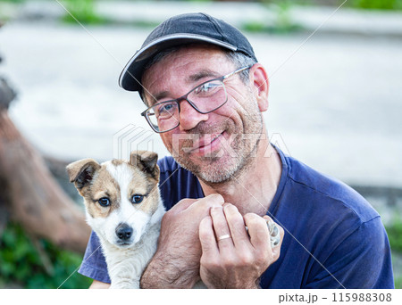 A very old man in glasses holds a dog next to him and hugs him like he is man's best friend. The dog is the most beautiful and it is small and attractive and playful. A very old man in glasses holds a dog next to him and hugs him like he is man's best friend. The dog is the most beautiful and it is small and attractive and playful. 115988308