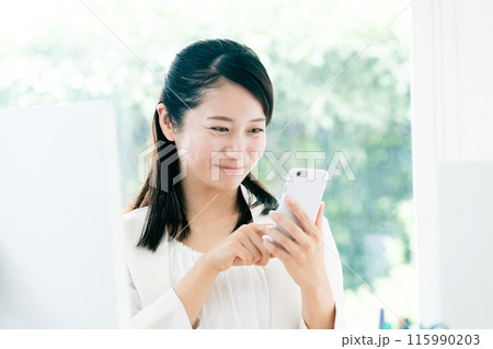 職場でスマートフォンを手に持つ若い女性 115990203