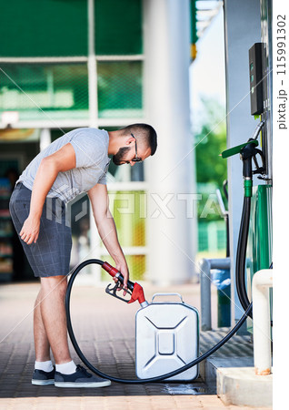 Side view of young driver filling canister with gasoline. Man refueling canister with fuel in case of unforeseen circumstances. Male adult with gasoline pump refueling cistern. Side view of young driver filling canister with gasoline. Man refueling canister with fuel in case of unforeseen circumstances. Male adult with gasoline pump refueling cistern. 115991302