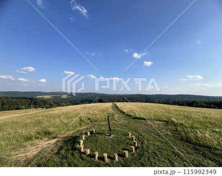 A sundial made of wooden bars in a field among greenery with a beautiful view 115992349