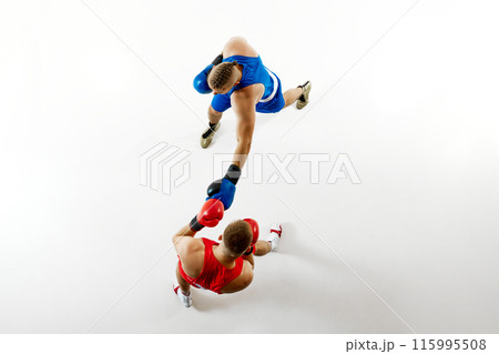 High-angle view of boxing bout with fighter dressed blue attire connecting punch with fighter in blue attire against white studio background. 115995508