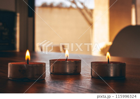 Small burning candles placed against window  115996324