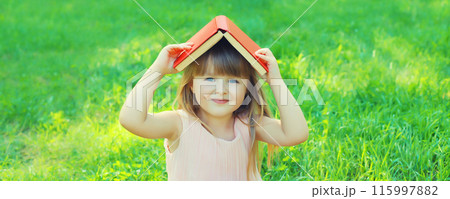 Happy little girl child reading book sitting on the grass in summer park Happy little girl child reading book sitting on the grass in summer park 115997882