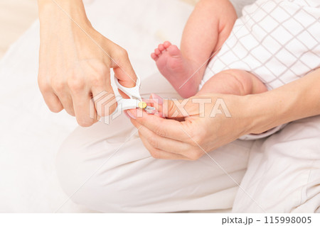 Mother trimming newborn baby toenails 115998005