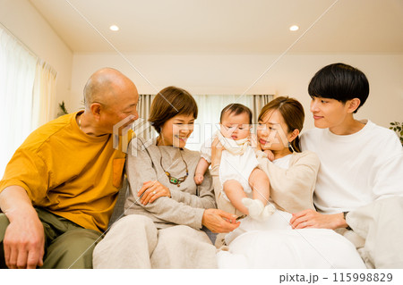 リビングで0歳児の赤ちゃんをあやし見守る両親と祖父母の3世代で5人の家族 115998829