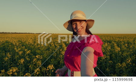 Young Woman Walking Through Field Next To Country Road. Leisure Activity On Outdoor Nature. Beautiful Brunette Woman In Pink Dress And White Hat On Colorful Rapeseed Fields. 115999698