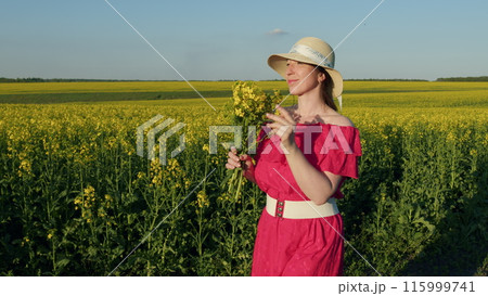 Beautiful Woman In Dress And Hat With Flower Bouquet, Enjoying Rapeseed Field. Portrait Of Young Brunette Female Wearing Hat With Rapeseed Bouquet. 115999741