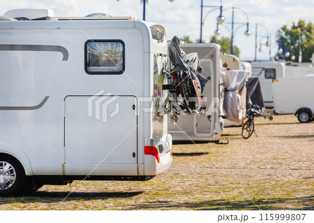 Many white modern campervan recreational motor home vehicles parked in row at camper park site Magdeburg city against Elbe river bridge. Motorhome campground stataion travel destination. RV lifestyle 115999807