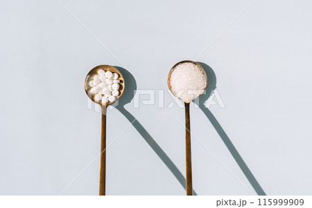 Two golden spoons contain sugar and sweetener on a blue background Two golden spoons contain sugar and sweetener on a blue background 115999909