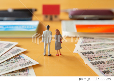 2つの通帳と印鑑、一万円札、家を前に立つ男性と女性のミニチュア、住宅ローン ペアローンのイメージ 2つの通帳と印鑑、一万円札、家を前に立つ男性と女性のミニチュア、住宅ローン ペアローンのイメージ 115999969