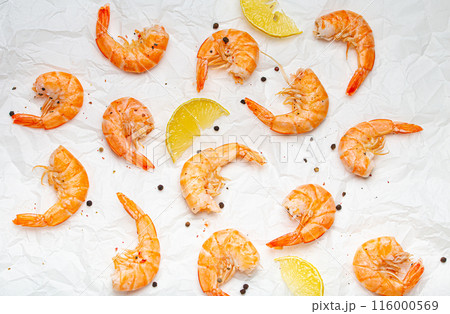 Roasted or grilled shrimps with seasonings and fresh lemon wedges top view on baking paper, healthy snack or appetizer. Seafood barbecue 116000569