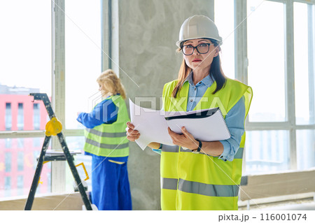 Industrial profession worker female in protective vest helmet working on construction. Industrial profession worker female in protective vest helmet working on construction. 116001074