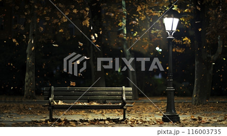 A park bench, softly lit by an antique streetlamp, stands serene amidst gently falling leaves at night. 116003735
