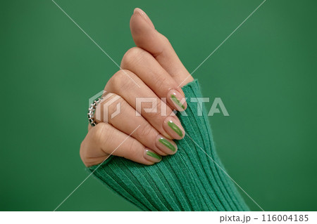Studio single color shot of neat short almond shaped nude fingernails decorated with green streak on emerald background, copy space 116004185