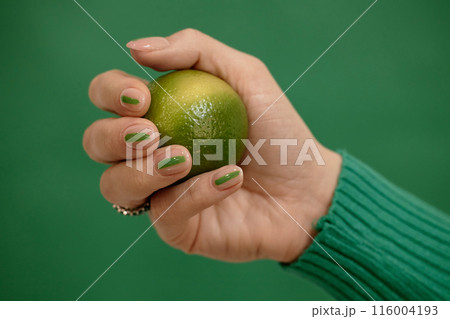 Studio shot of stylish neutral female nails designed with green streak on emerald background in composition with fresh lime, copy space Studio shot of stylish neutral female nails designed with green streak on emerald background in composition with fresh lime, copy space 116004193